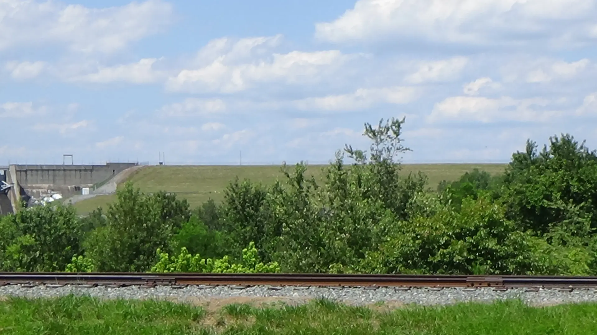 Photo of the right side of the dam and the grassy leading up to it, with a railroad in the foreground