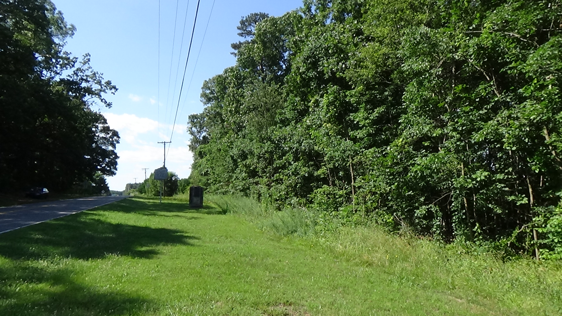 Photo up a two-lane rural road with the monument in the distance and trees on the right
