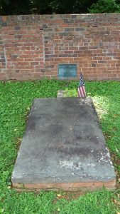 Photo of a grave-sized concrete slab on top of a low brick foundation, with a marker and brick wall behind