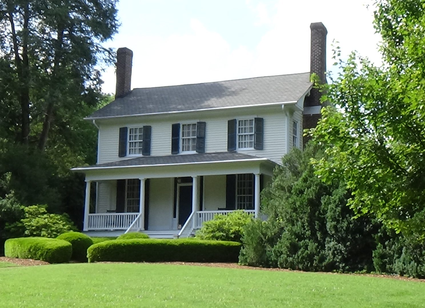 Photo of a two-story white, wood-sided home with a first-floor porch and chimneys on each end