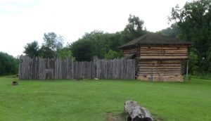 Photo of a two-story log blockhouse and wall of vertical logs