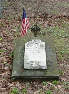 Photo of a tombstone marked by a small American flag and veteran marker
