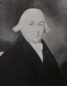 Photo of a man in a wig, black coat, and white cravat