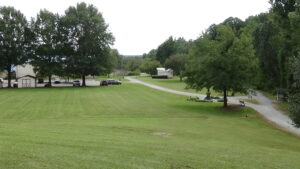Photo looking down a grassy slope, with a trail on the right splitting into two, and buildings and trees in the background