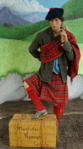 Photo of a mannequin wearing a red-plaid Highlander kilt, with a mural of the Scottish highlands behind