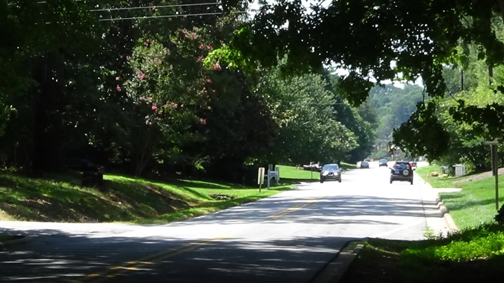 Photo looking down two-lane city road with trees and grass along the left side