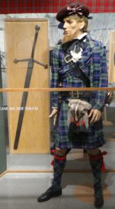 Photo of a mannequin in kilt and a broadsword under glass behind him