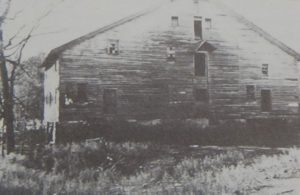 Old black-and-white poto of a large wooden building with three doors in a vertical line in the center