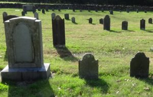 Photo of a larger gravestone on the left and smaller ones to the right, with more behind