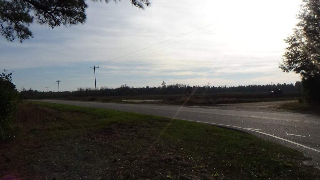 Photo of a two-lane road passing in front of a farm field