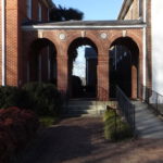 Photo of a covered walkway between two brick buildings with three arches
