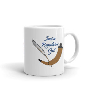 White mug with drawings of a quill and powder horn and the words, "Just a Regulator Gal"