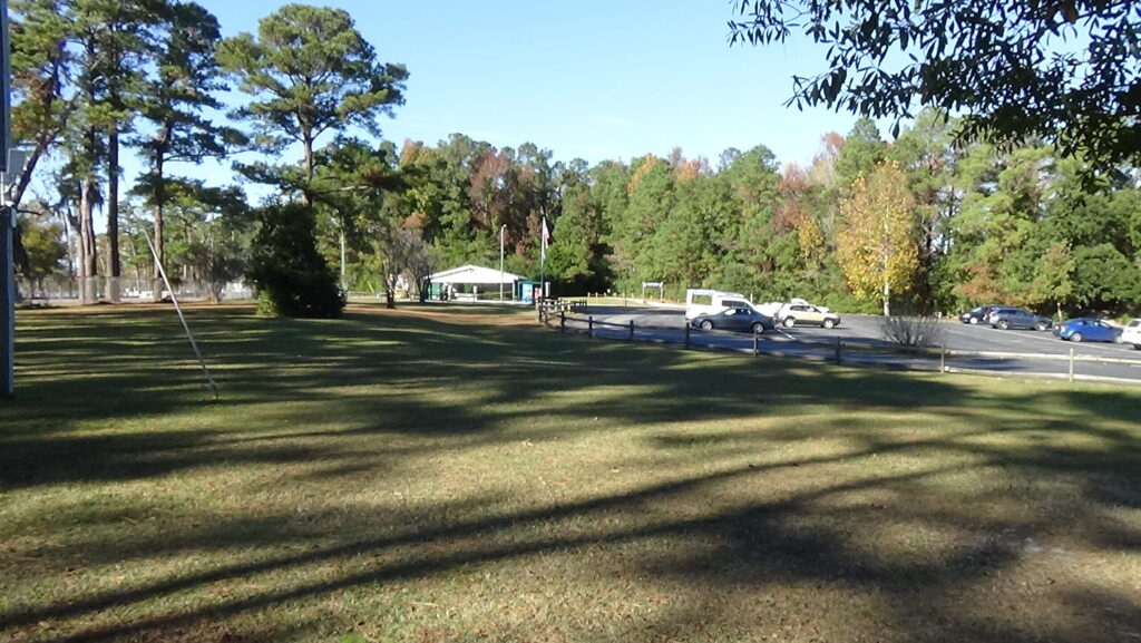 Photo of a grassy area with a parking lot in the distance and trees in the background