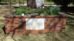 Photo of a grave in a raised brick planter with a marble plaque on front