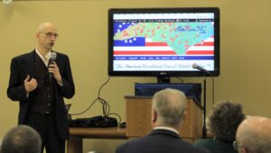 Photo of a bald guy with glasses in a blue suit giving a presentation