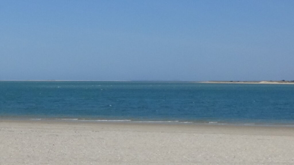 Photo of open water above a beach with a sandy strip on the left at the horizon
