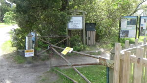 Photo of a gate across a trail with signs and bushes in the background