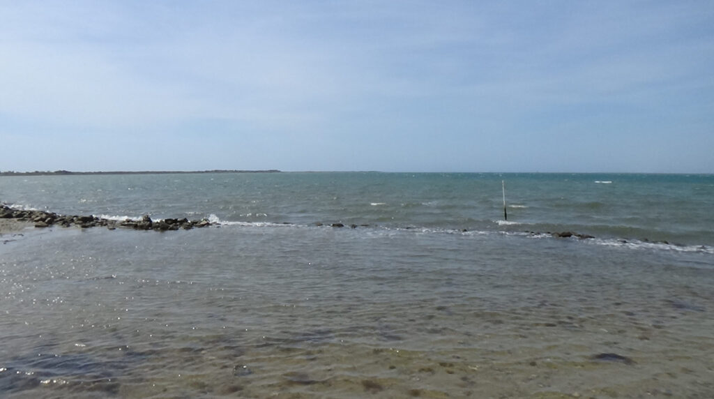 Photo of open water with a line of land intruding the horizon from the left, and a then shore on the right