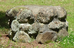 Photo of a round monument of stones, the size and shape of a water well, surrounded by grass